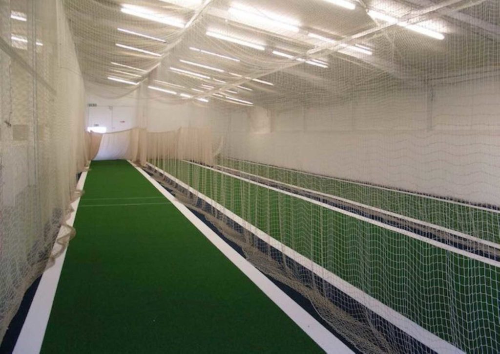 A well lit indoor space with cricket training nets.